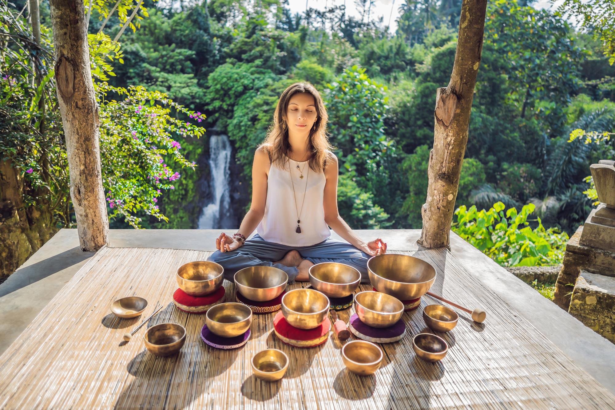 woman-playing-tibetan-singing-bowl-while-sitting-yoga-mat-against-waterfall